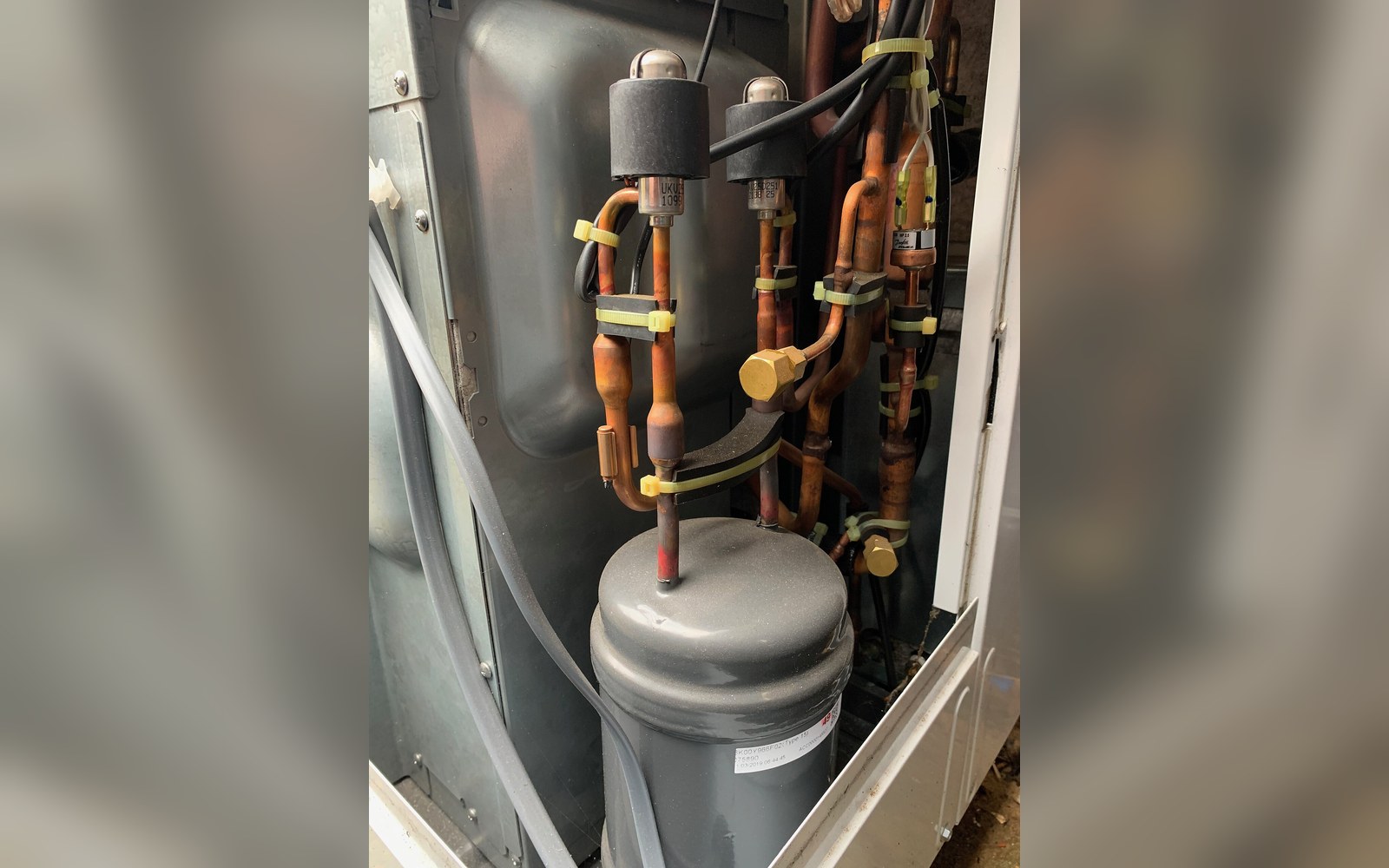 A heat pump unit against a rendered wall with flow and return pipework