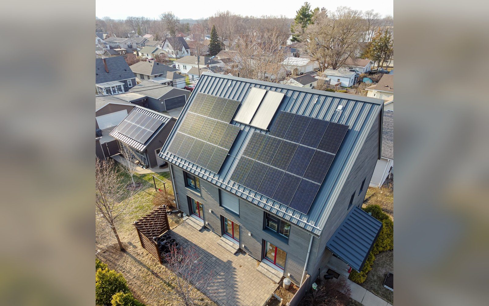 Aerial view of a house with a steep solar-paneled roof in a residential neighborhood